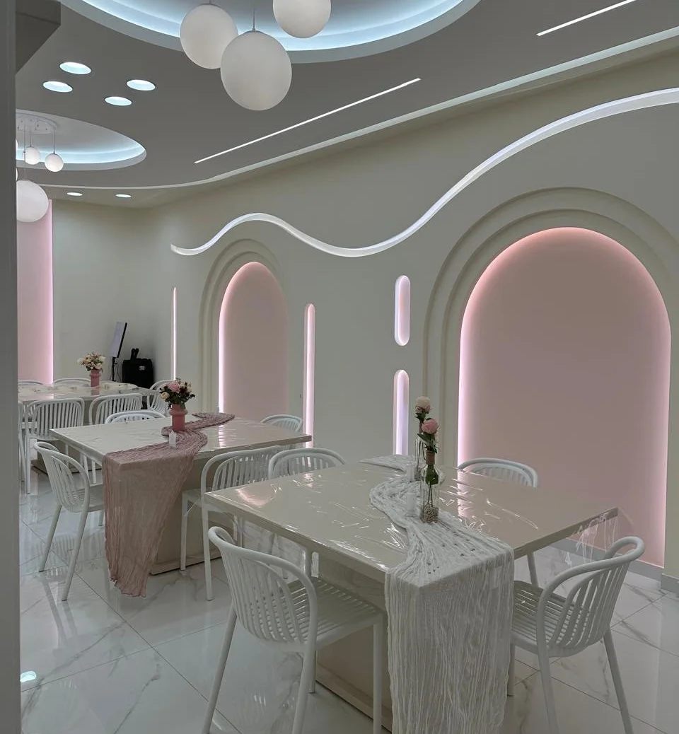 Pink-lit arches and a wavy light line over styled tables at Cakies